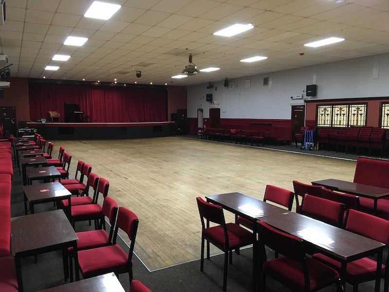 The venue, a dance hall with a large wooden floor and bench seats,
                     tables and chairs around the sides and at the back, and a stage at the front