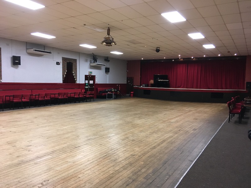The venue, a dance hall with a large wooden floor and bench seats,
                     tables and chairs around the sides, and a stage at one end